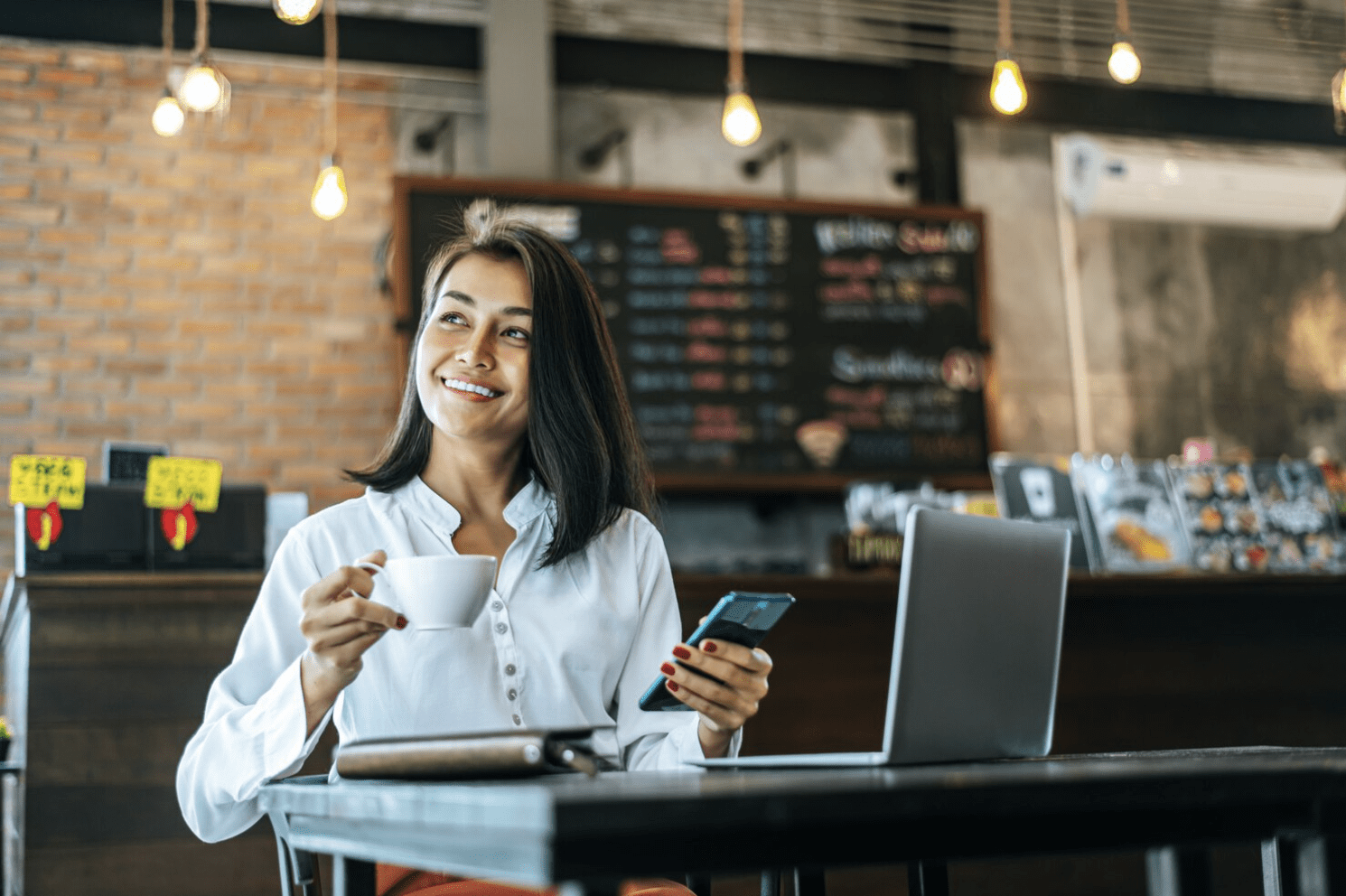 A small business owner is drinking coffee while working at her cafe. Merchant payment solutions can improve merchant experiences and loyalty, whether its resilient payment processing solutions to disbursements.